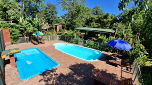 A rectangular swimming pool with a brick deck, surrounded by lush greenery and a covered seating area with umbrellas. - Estrella del Monte (Puerto Iguazú)