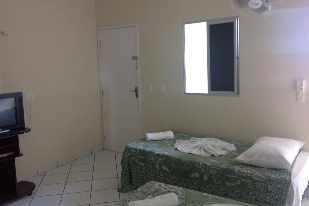 A small, clean room with a bed, a TV, and a window.