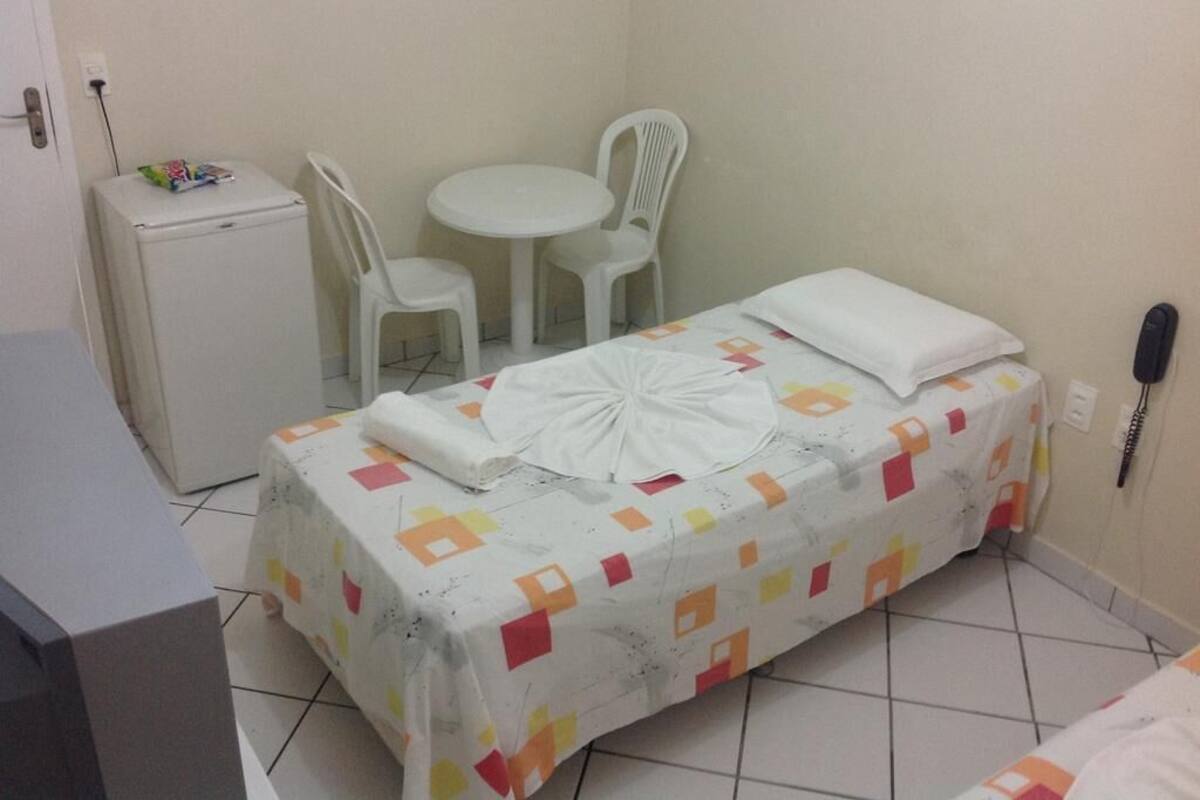 A small hotel room with a bed, a desk, a chair, and a refrigerator.