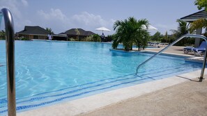 Una piscina al aire libre, sombrillas, sillones reclinables de piscina