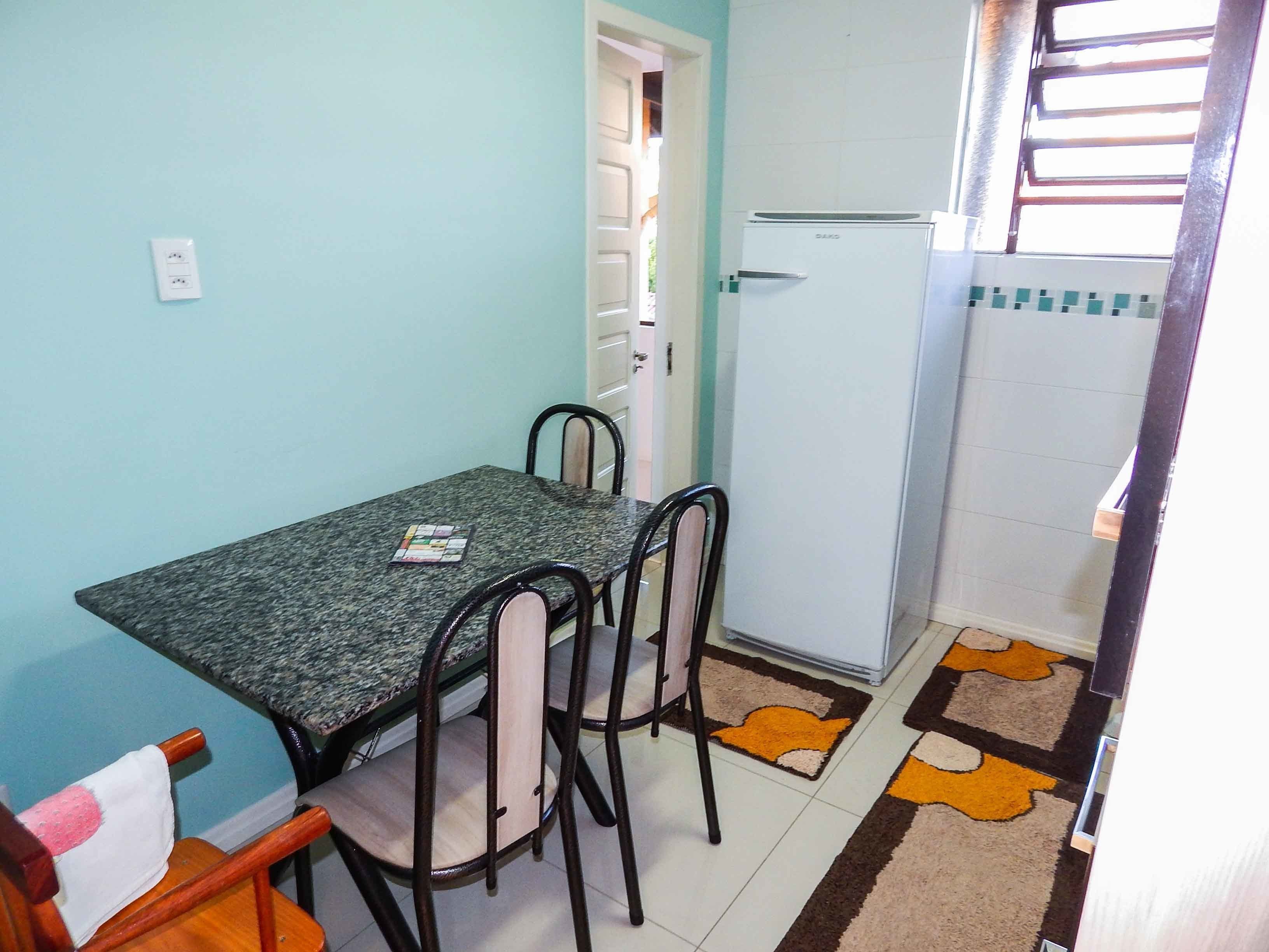A small kitchen with a dining table, chairs, a refrigerator, and a patterned rug.