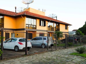 A two-story building with a yellow facade, satellite dishes, and a gated parking area with cars. - Morada do Centro Apartamento (Canela)
