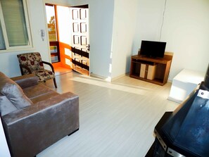 A living room with a sofa, a television on a wooden stand, and a door leading outside. - Morada do Centro Apartamento (Canela)