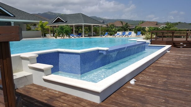 A swimming pool with a wooden deck, lounge chairs, and a view of mountains. - Ocho Rios Villa at Coolshade X (St. Ann's Bay)