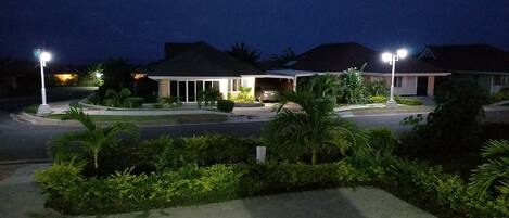 A residential area at night with houses, street lighting, and well-maintained landscaping.