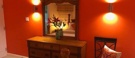 A room with a wooden dresser, a chair, and a mirror with wall sconces.