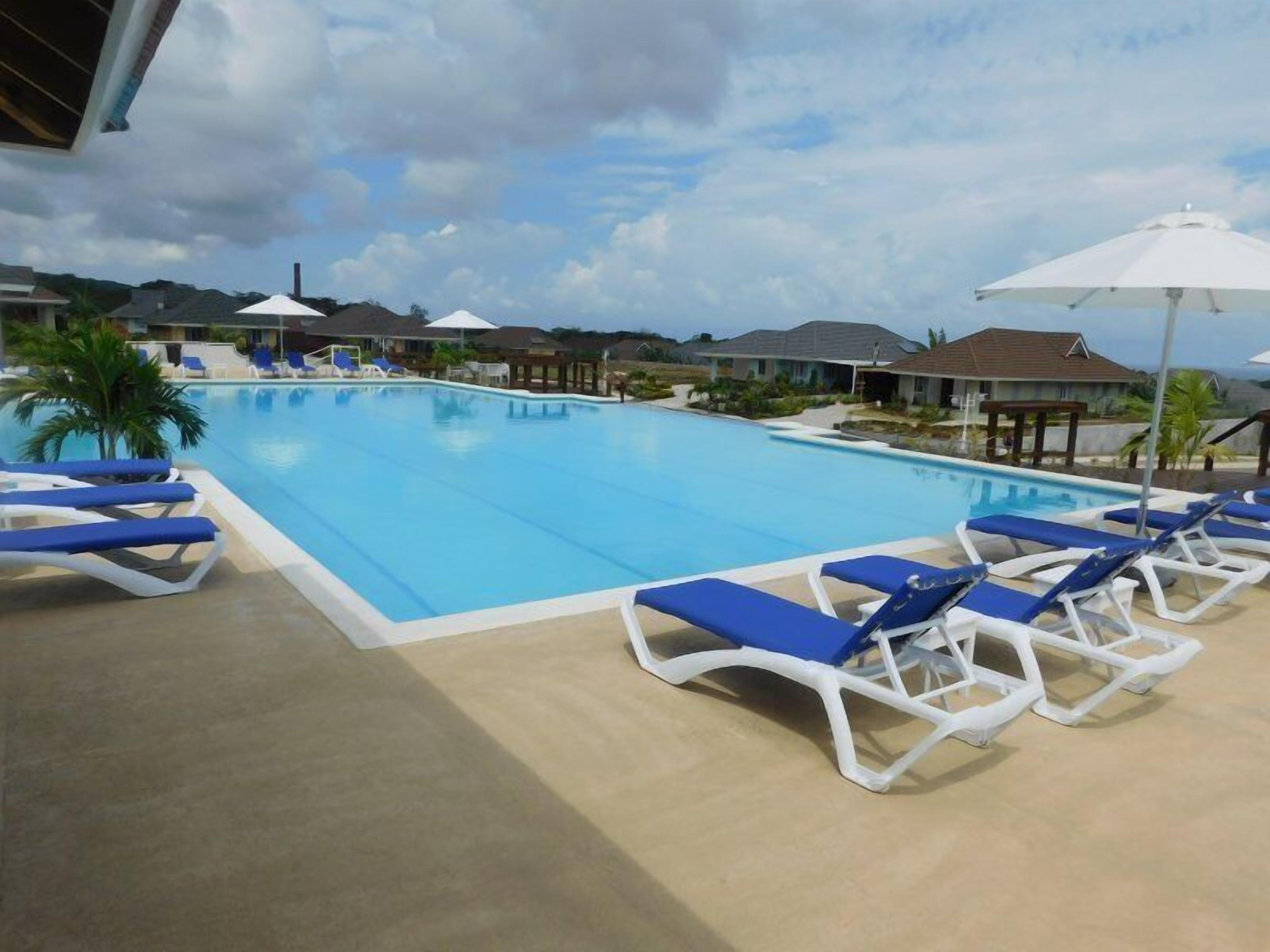 A swimming pool with blue water, surrounded by lounge chairs and umbrellas.