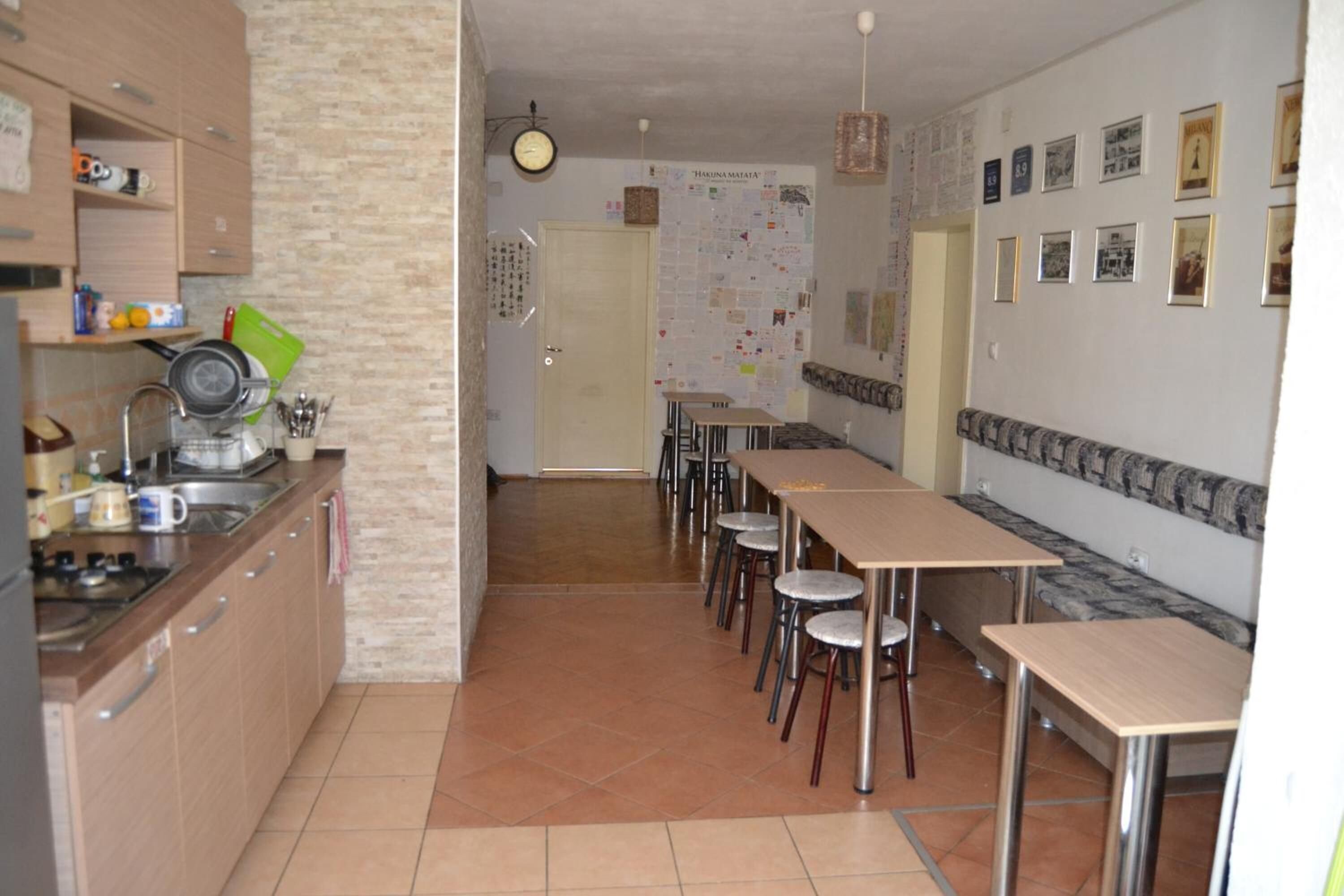 A kitchen with a dining area, featuring a long table and chairs, a stove, and various kitchen utensils.