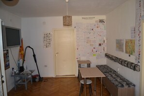 A room with a wooden floor, a desk, a bench, a door, and a wall covered with papers and notes. - Hostel Valentin 2 (Skopje)