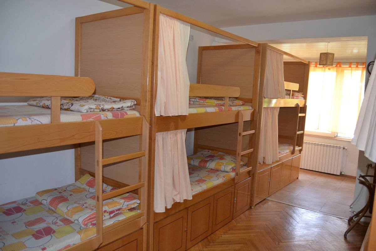 Dormitorio con literas de madera, un radiador y una ventana con cortinas.