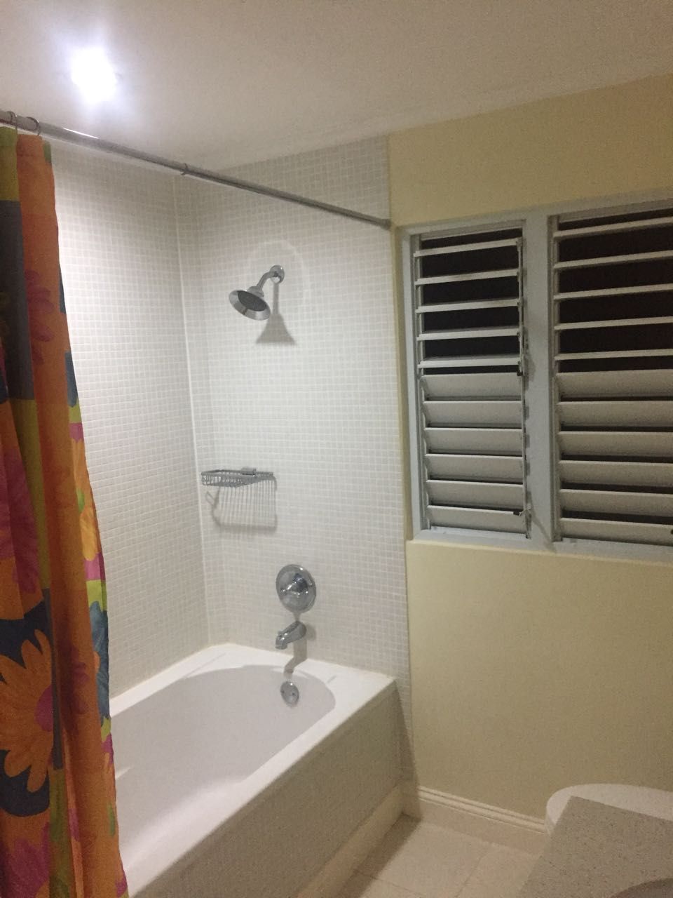 A bathroom with a bathtub, a shower curtain, a towel rack, and a window with blinds.