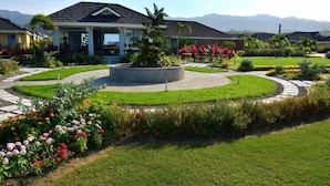 Una zona residencial con casas, un jardín circular con maceta central y una vista despejada de montañas al fondo.