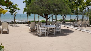 Un espacio de descanso frente al mar con una mesa y sillas, un árbol que da sombra y vista al océano.