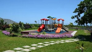 A playground with slides and climbing structures, surrounded by a garden with flowers and a paved path. - Ocho Rios Villa at the Palms V (St. Ann's Bay)