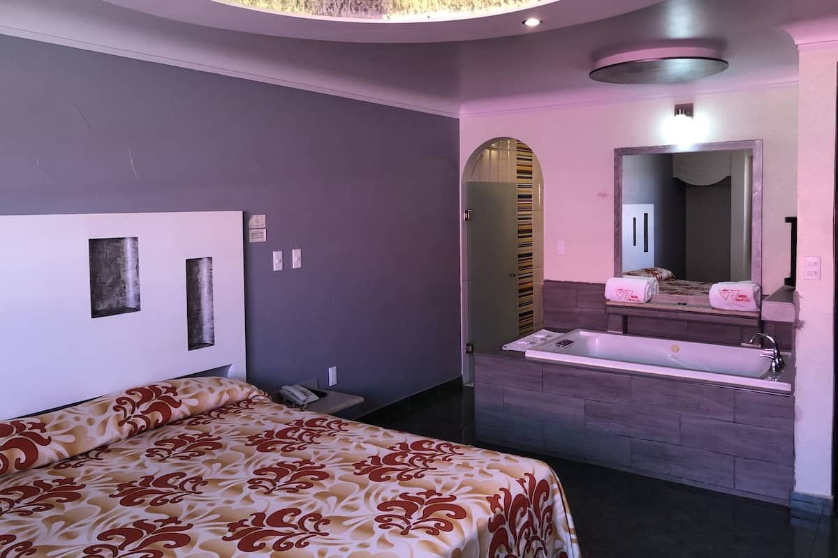 Una habitación de hotel moderna con una cama grande, un tocador empotrado con espejo y una zona de ducha separada.