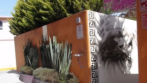 A building with a mural of a lion's face, a gated entrance, and a row of tall plants.