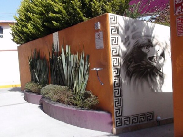 A building with a mural of a lion's face, a gated entrance, and a row of tall plants.