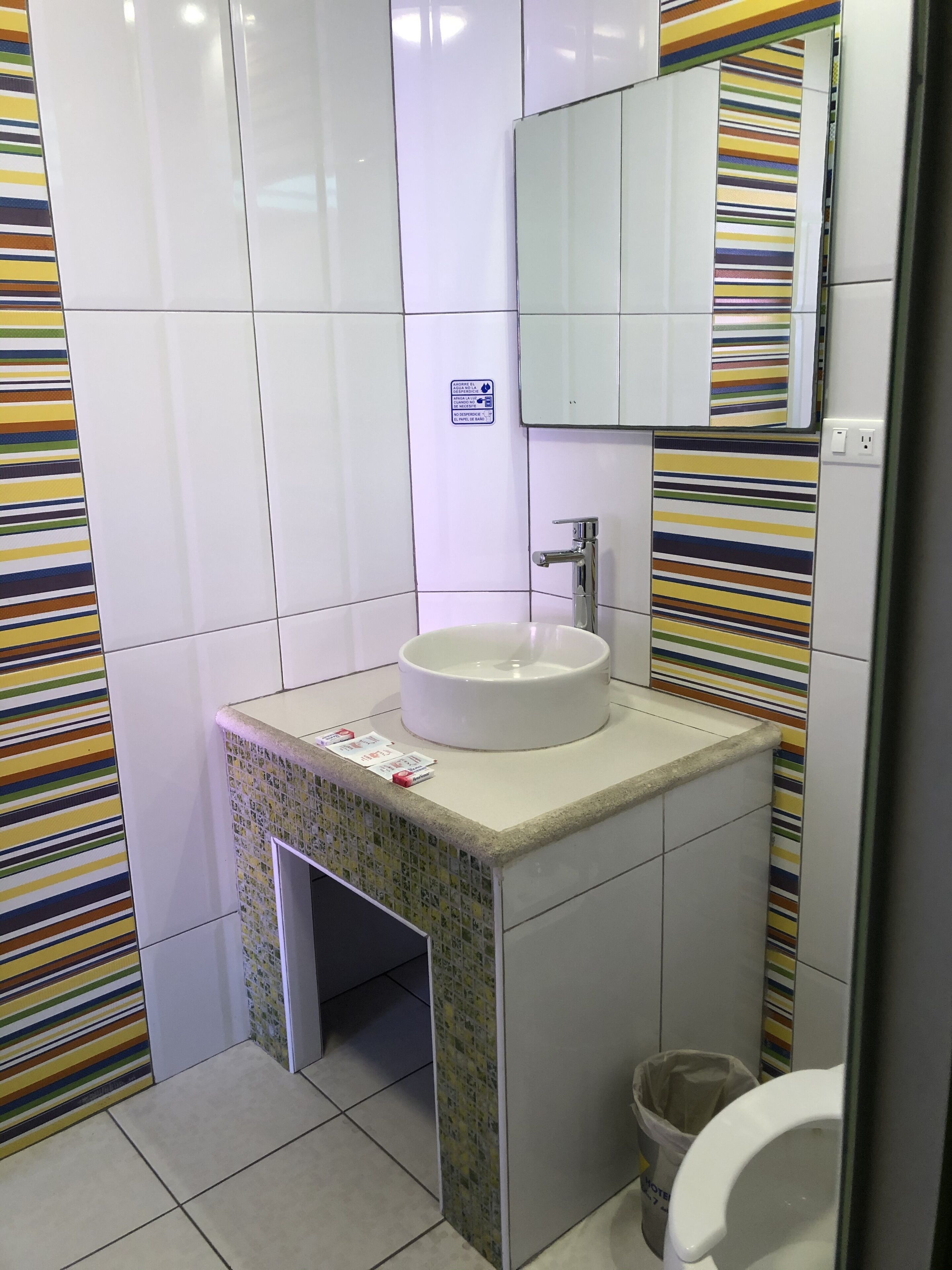 A bathroom with a white sink, a mirror, and striped tiles on the walls.