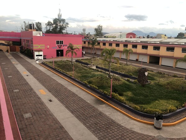 Un edificio con fachada rosa, un estacionamiento y un jardín ajardinado con palmeras.