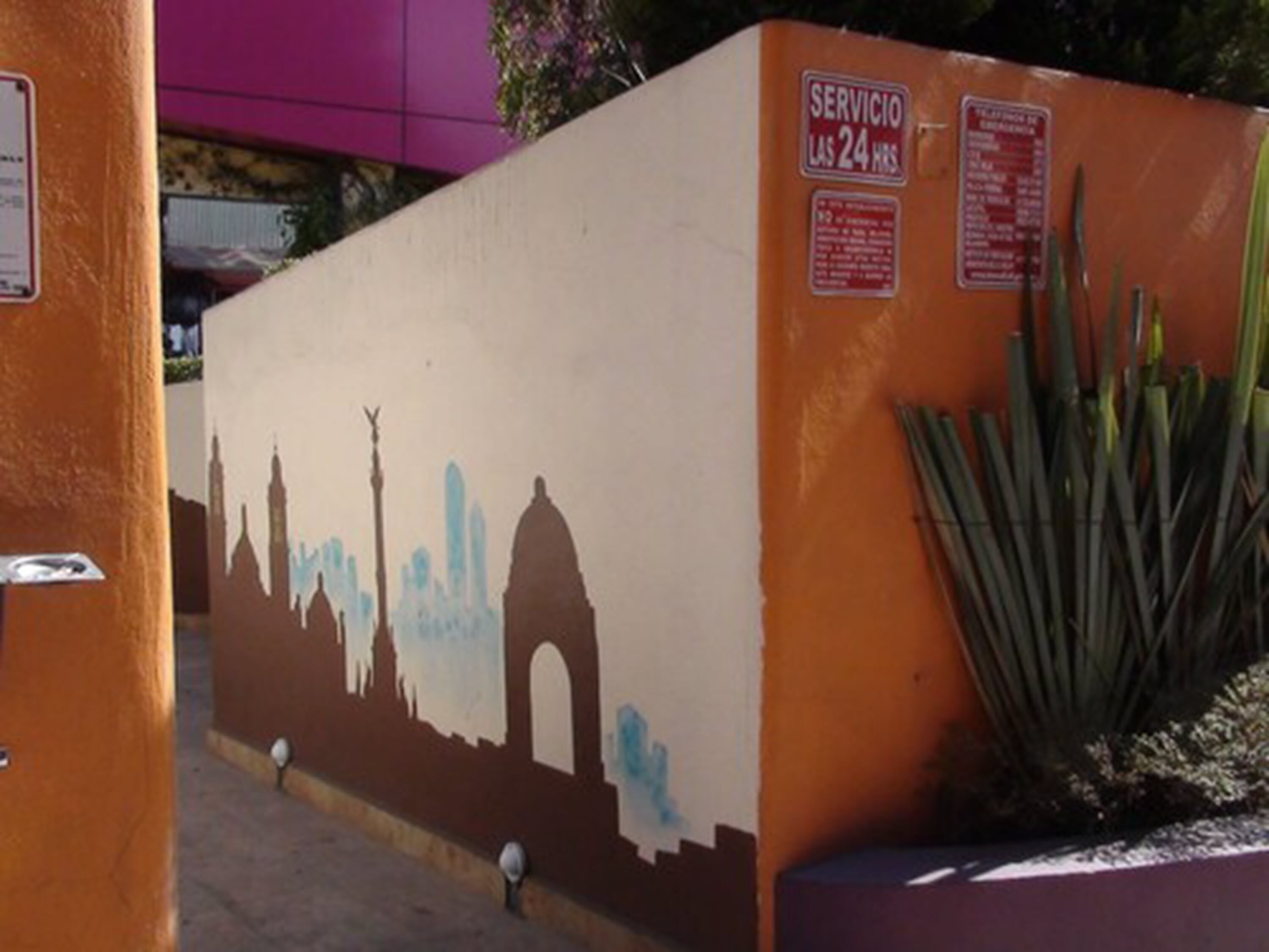 Un mur orné d’une fresque représentant une vue panoramique d’une ville, d’un panneau indiquant les services disponibles et d’une plante.