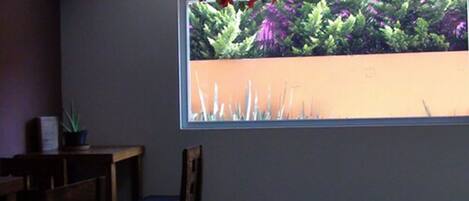 Una habitación con ventana que da a un jardín, una silla de madera y una mesita con una planta en maceta.