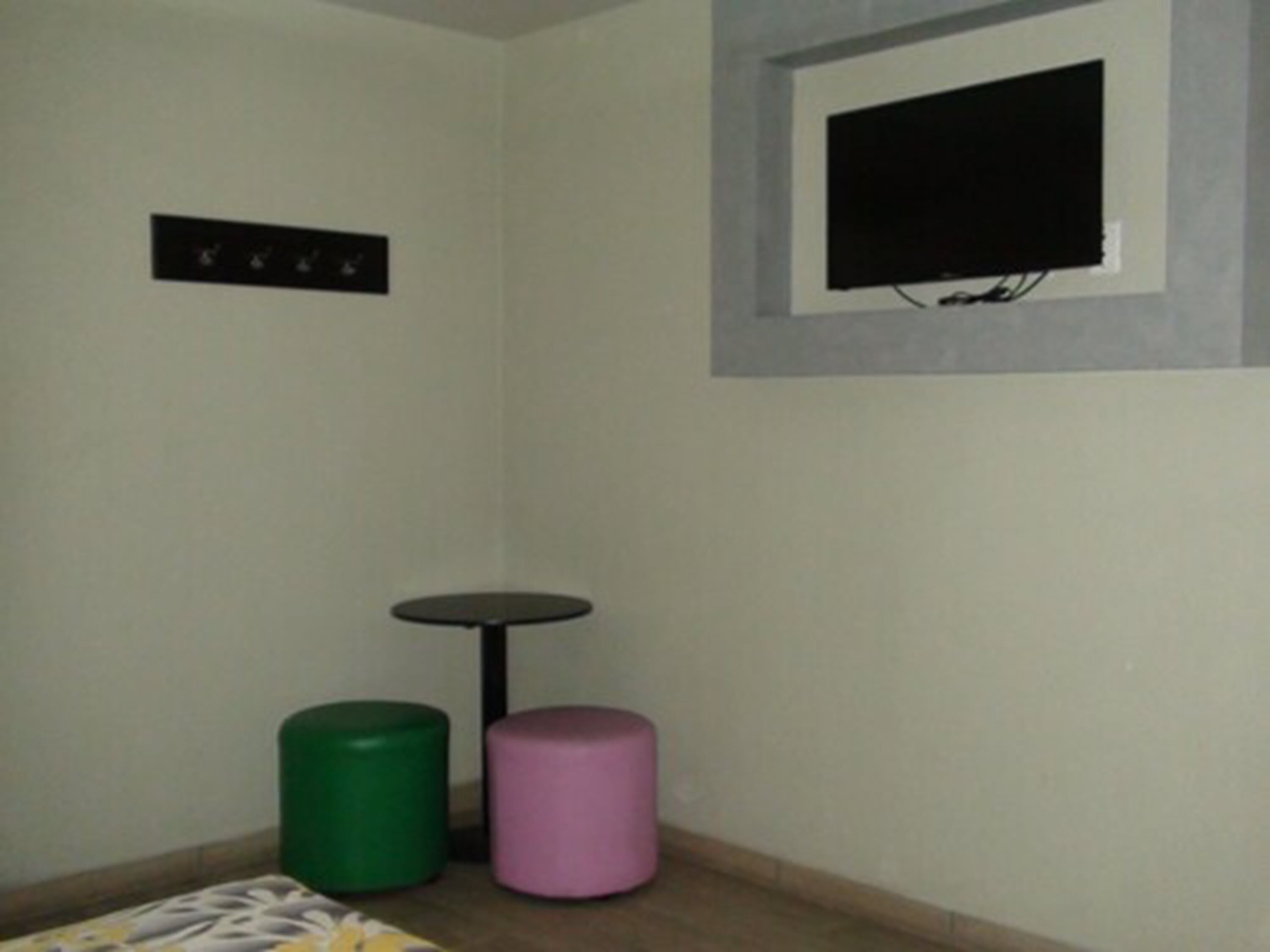 A small room with a bed, a television mounted on the wall, and two cylindrical stools.