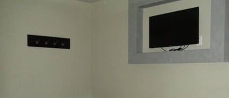 A small room with a bed, a television mounted on the wall, and two cylindrical stools.