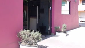 A building with a pink exterior, a glass entrance, and potted plants in front.