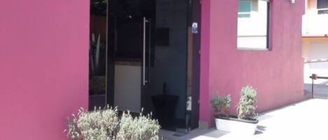 Un edificio con fachada rosa, entrada de vidrio y plantas en macetas al frente.