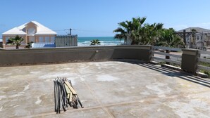 A rooftop with a concrete floor, a pile of metal rods, and a view of the ocean and buildings.