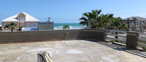 A rooftop with a concrete floor, a pile of metal rods, and a view of the ocean and buildings.