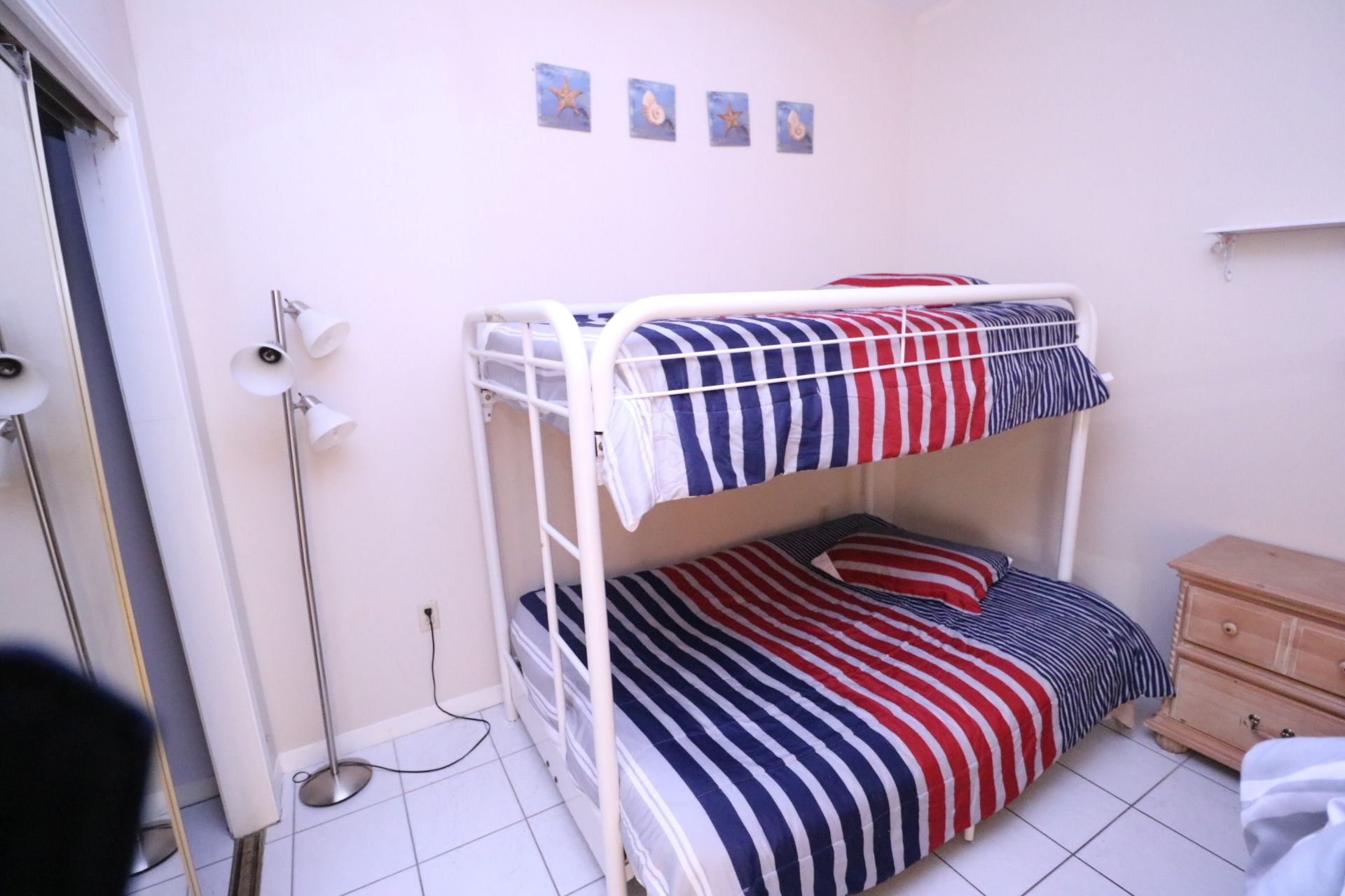A bunk bed with striped bedding, a bedside table, a lamp, and a small dresser.
