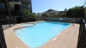 A rectangular swimming pool with a curved section, surrounded by a black metal fence.