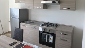 Cocina compacta equipada con refrigerador, estufa, horno y una pequeña zona de comedor con una silla y mesa.