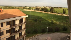 Un edificio de varios pisos con balcones, vista a un campo verde y edificios al fondo.
