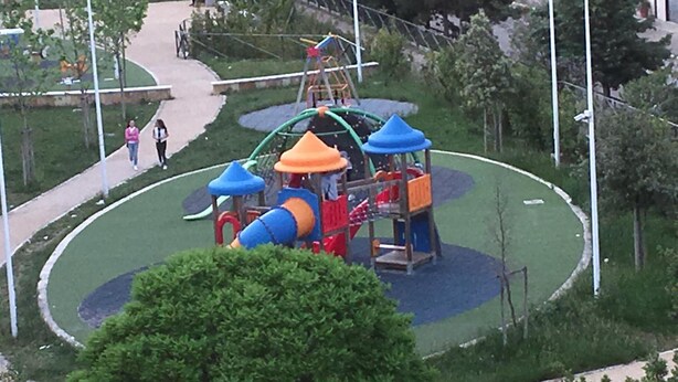 Un parque infantil con toboganes y estructuras de escalada, rodeado de un área ajardinada con árboles y un sendero para caminar.