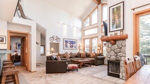 Una sala de estar amplia con chimenea de piedra, ventanas grandes y un rincón de descanso acogedor.