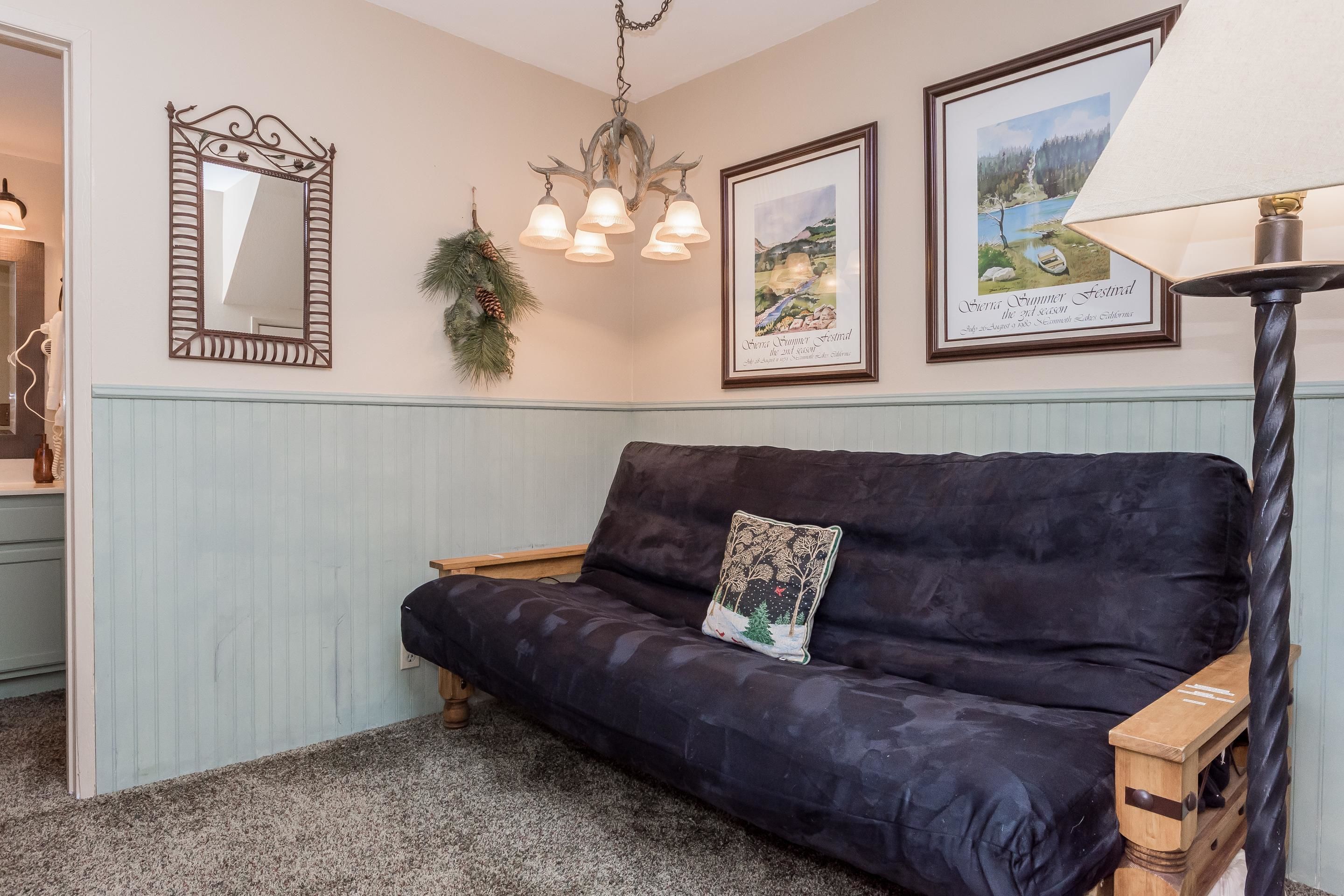A dark blue sofa with a decorative pillow, a wall-mounted mirror, a chandelier, and framed pictures on the wall.
