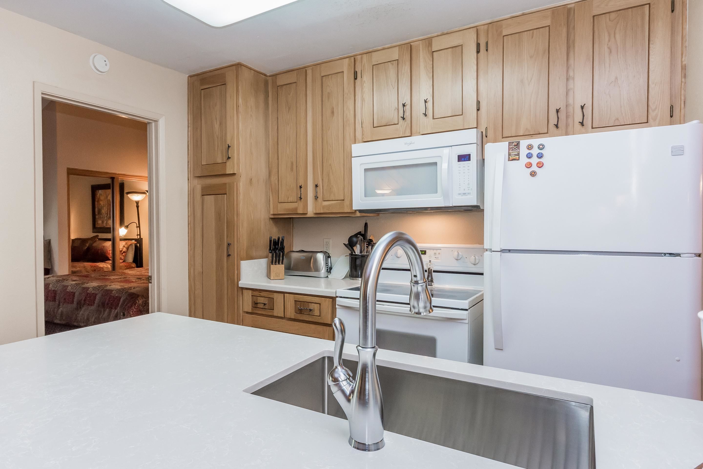 Een moderne keuken met houten kastjes, een RVS spoelbak, een witte koelkast en een magnetron.