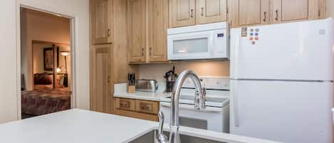 A modern kitchen with wooden cabinets, a stainless steel sink, a white refrigerator, and a microwave.