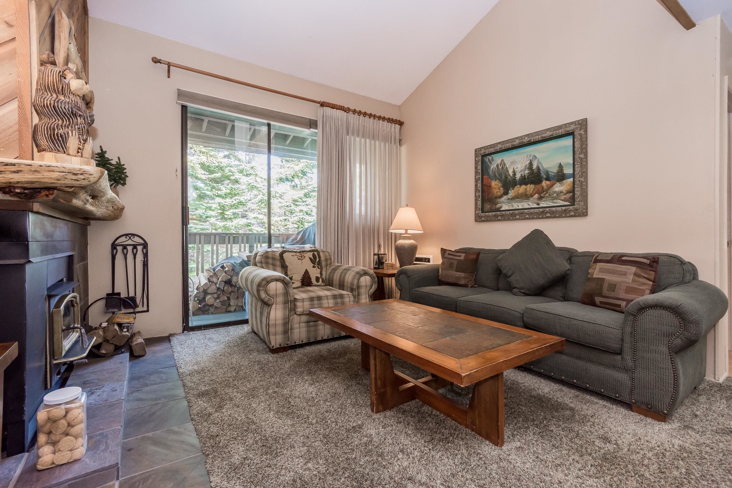 A cozy living room with a fireplace, a large window with curtains, a sofa, a coffee table, and a painting on the wall.