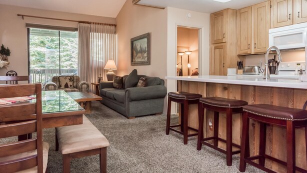 A cozy living room with a glass-top coffee table, a sofa, and a dining area with wooden chairs and a bench. - Crestview B46 (Mammoth Lakes)