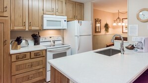 A modern kitchen with wooden cabinets, a white microwave, a refrigerator, a stove, and a sink. - Crestview B46 (Mammoth Lakes)