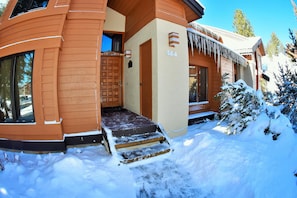Uma cabana de madeira com entrada coberta de neve e degraus que levam à porta.