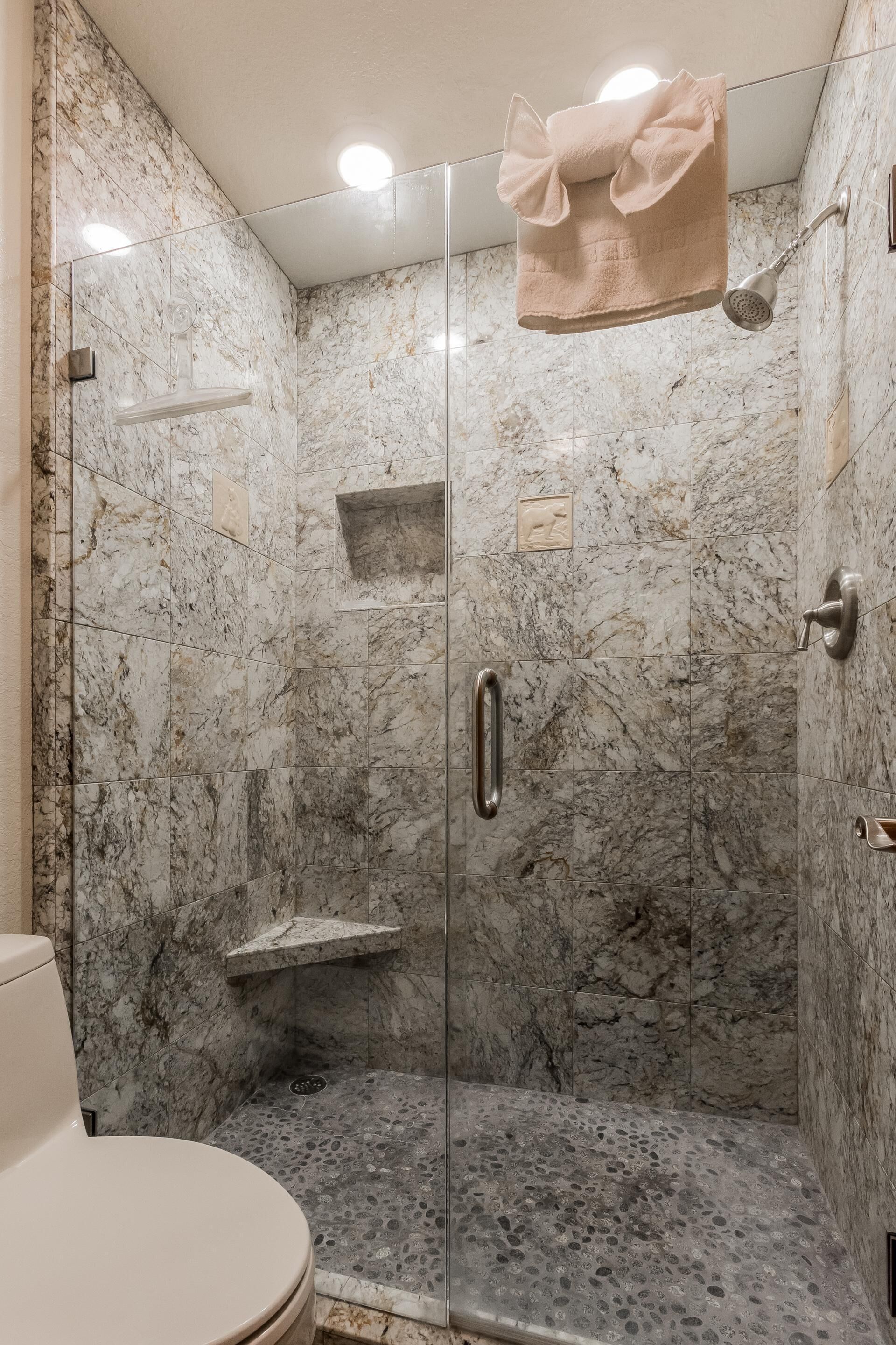 A bathroom with a marble shower enclosure, a glass door, and a towel hanging on the showerhead.