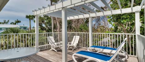 A covered outdoor area with a wooden deck, white railings, and lounge chairs.