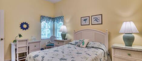 A bedroom with a bed, two nightstands, a chair, a desk, and a window with curtains.