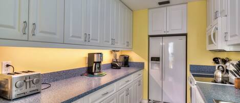 Una cocina con armarios blancos, microondas integrado, refrigerador de acero inoxidable, cafetera y tostadora.