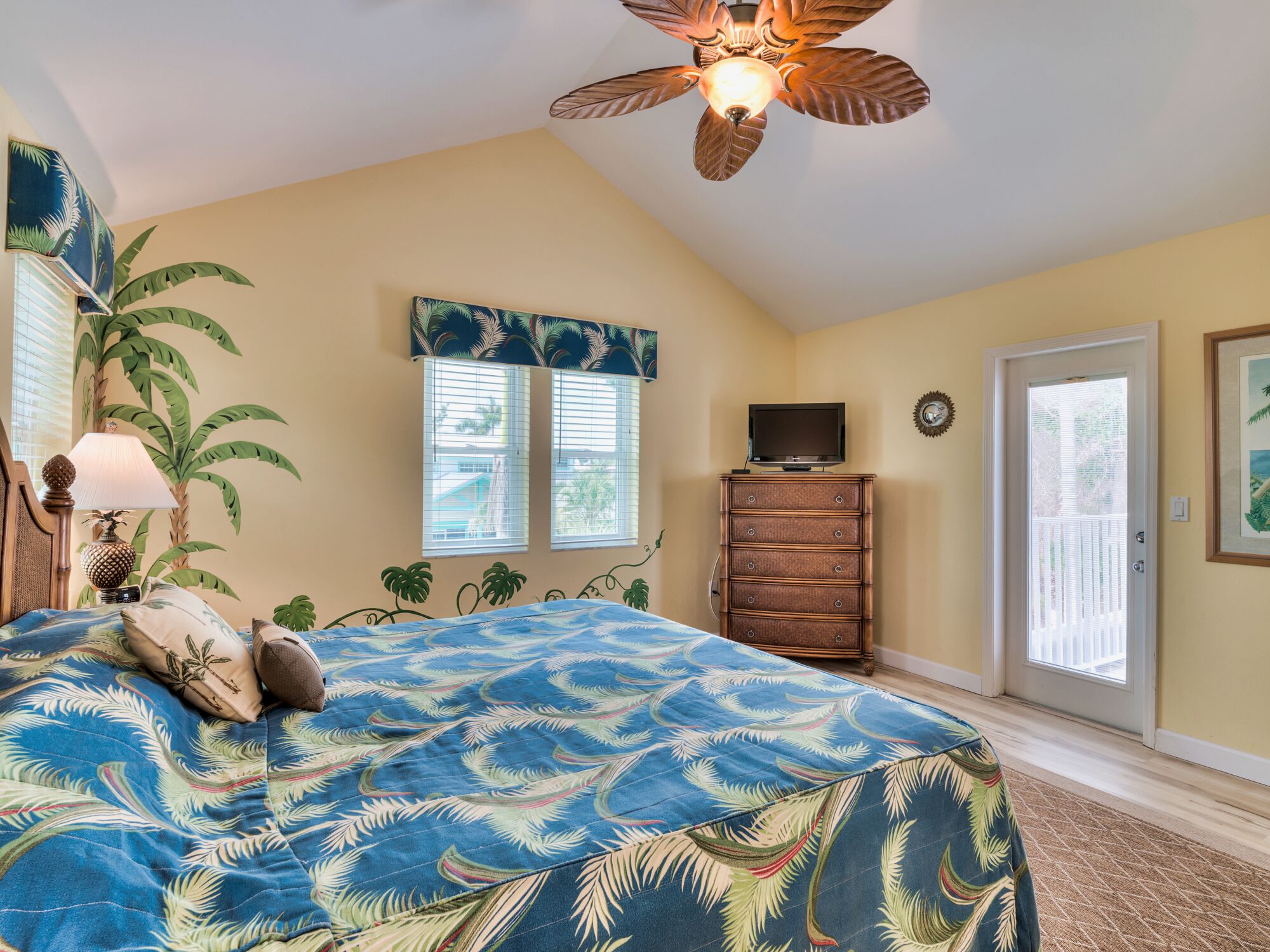 Une chambre à coucher comprenant un lit, un ventilateur de plafond, une commode, un téléviseur et une porte donnant sur une vue agréable.