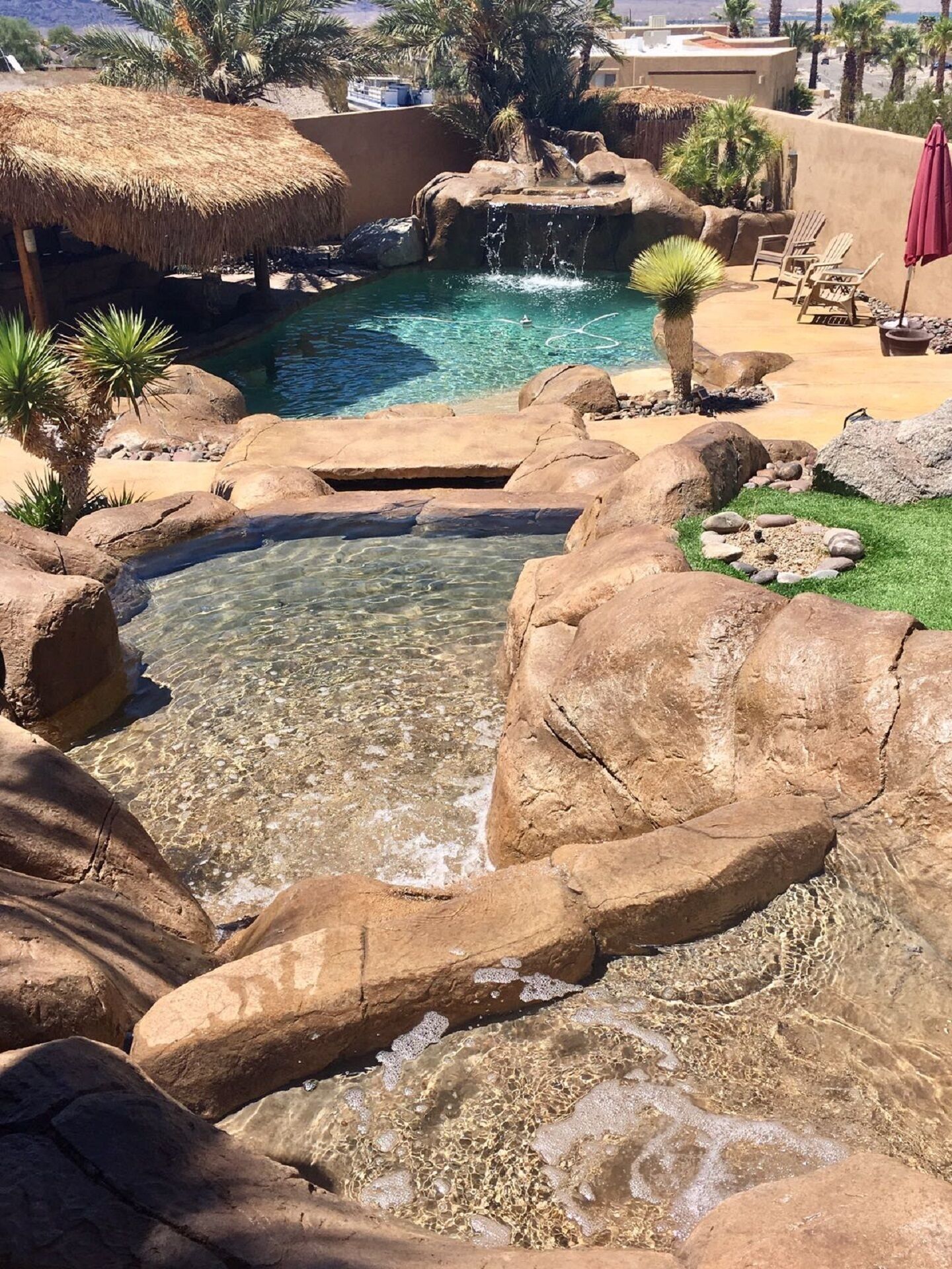 A clear pool with a waterfall feature surrounded by rocks and palm trees.